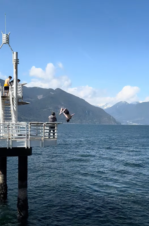 A man doing a backflip dive, jumping from a bridge into the sea